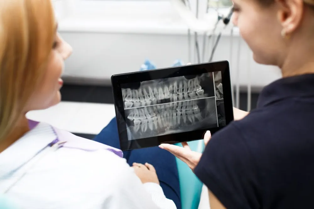 A dentist showing a patient a dental X-ray on a tablet