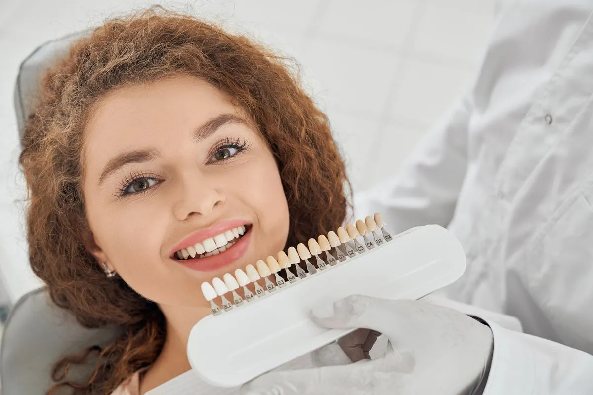 A dentist holding a shade guide next to a patient's teeth